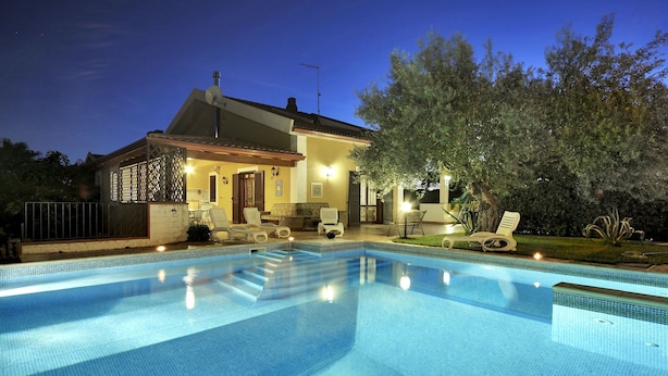 A swimming pool with lounge chairs and a patio area in front of a house at night. - Wonderful private villa for 8 people with private pool, WIFI, A/C and TV (Marina Di Ragusa)
