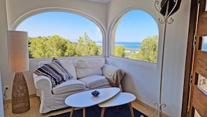 A cozy corner with a white sofa, a small round table, and a view of the sea through arched windows. - Doble Diez - Denia, Costa Blanca (Denia)