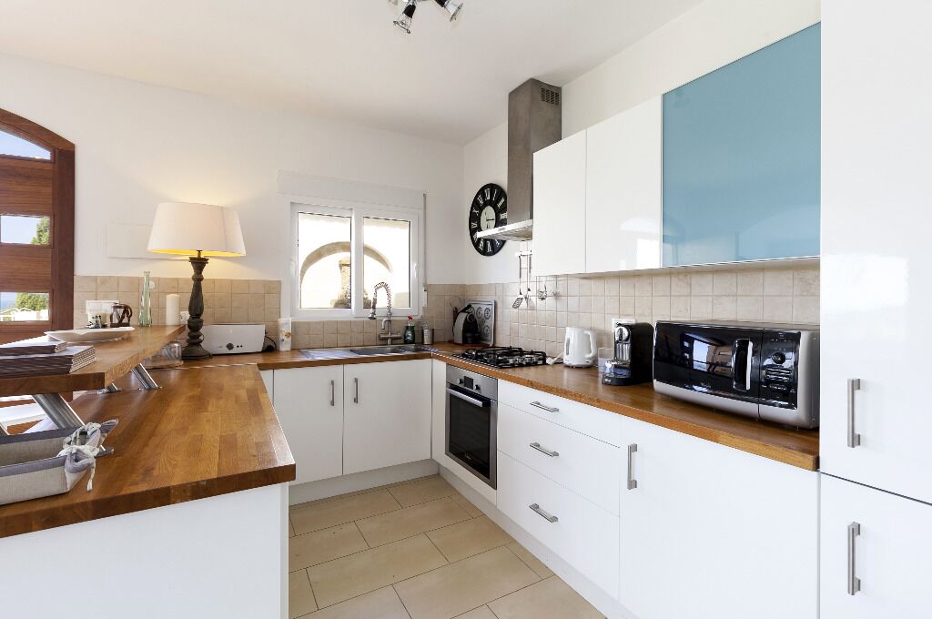 A modern kitchen with white cabinets, a wooden countertop, a stove, a microwave, and a window with a view.