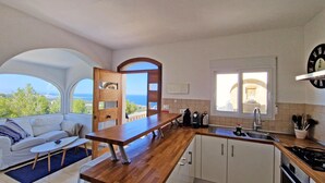 A modern kitchen with a wooden countertop, white cabinets, and a view of the sea through large windows. - Doble Diez - Denia, Costa Blanca (Denia)