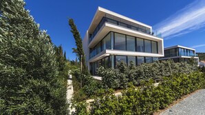 A modern two-story building with large glass windows and a flat roof, surrounded by dense greenery. - Luxury Apartment the Ocean Dream V (Primošten)
