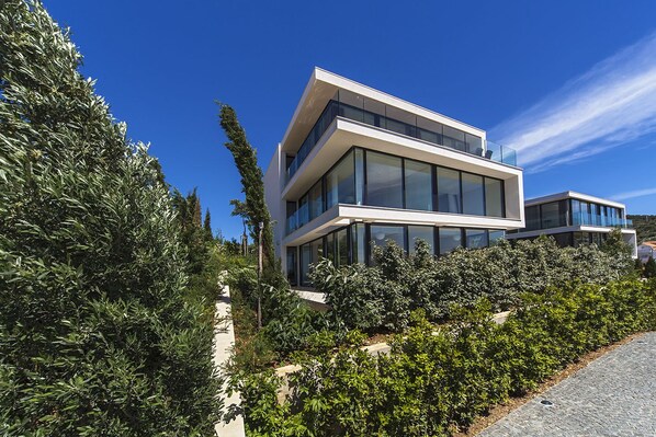 Un bâtiment moderne à deux étages, doté de grandes fenêtres en verre et d’un toit plat, entouré d’une végétation luxuriante.