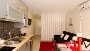 Une cuisine compacte dotée d’appareils électroménagers modernes, un coin repas avec une nappe rouge et un mur à rayures en arrière-plan.