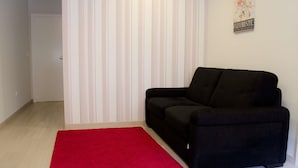 Un salon avec un canapé noir, un tapis rouge et un mur à rayures.