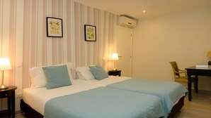 Une chambre d’hôtel avec deux lits, un papier peint à rayures, des œuvres d’art encadrées, un appareil de climatisation, un bureau avec une chaise et des lampes de chevet.