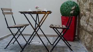 Un petit espace extérieur aménagé avec une table et deux chaises, un pot de fleurs et un mur en pierre.