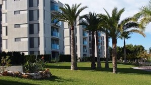 Un immeuble moderne à plusieurs étages, doté de balcons, entouré de pelouses bien entretenues et de palmiers.