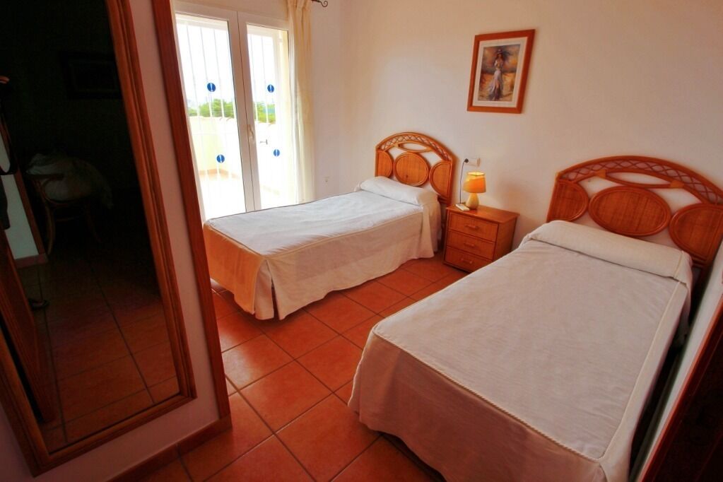 A room with two single beds, a wooden nightstand with a lamp, and a painting on the wall.