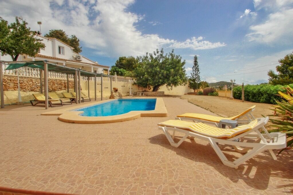 A swimming pool with lounge chairs, a covered seating area, and a stone wall.