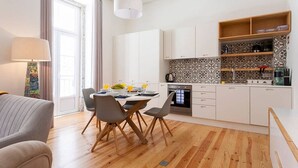 Una cocina moderna con armarios blancos, una zona de comedor con mesa y sillas, y piso de madera.