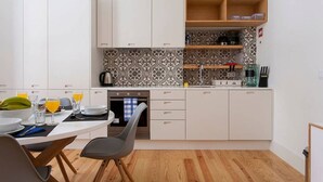 Una cocina compacta con armarios blancos, un salpicadero estampado y un estante de madera.