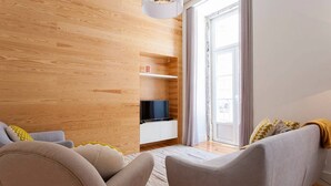 Una sala de estar moderna con una pared de madera, un televisor sobre un estante blanco y un sofá con cojines.