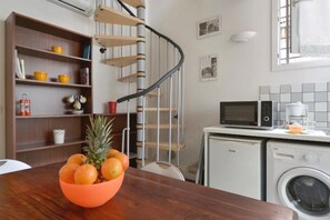 A compact kitchen with a wooden spiral staircase, a washing machine, and a microwave.