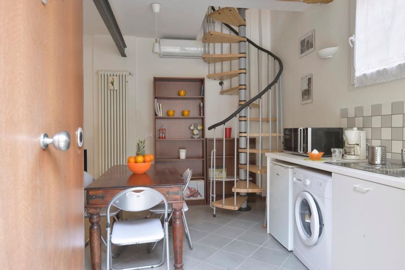 A compact kitchen with a wooden table, chairs, a built-in washing machine, and a spiral staircase.