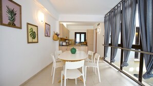 Una cocina moderna con armarios blancos, una mesa de comedor con sillas y un amplio ventanal con cortinas.