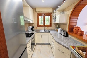A compact kitchen with a central island, a sink, and a window with a view of greenery. - Chrisuli - well furnished villa with panoramic views in Moraira (Benimeit)