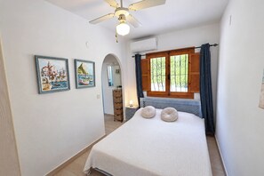 A bedroom with a bed, a ceiling fan, a window with curtains, and two framed pictures on the wall. - Chrisuli - well furnished villa with panoramic views in Moraira (Benimeit)
