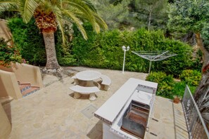 An outdoor patio with a grill, a round table, and benches. - Chrisuli - well furnished villa with panoramic views in Moraira (Benimeit)
