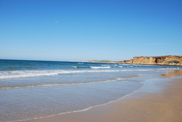 A beach with waves, a clear sky, and a distant lighthouse.