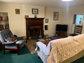 A living room with a fireplace, a television, a bookshelf, and a comfortable seating area. - Pond Cottage, Carmichael Country Cottages. Pets welcome. (Biggar)