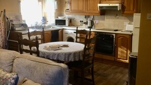A compact kitchen with wooden cabinets, a dining table, and a built-in oven. - Pond Cottage, Carmichael Country Cottages. Pets welcome. (Biggar)