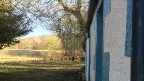 A rustic building with a wooden bench outside, surrounded by trees and a field. - Pond Cottage, Carmichael Country Cottages. Pets welcome. (Biggar)