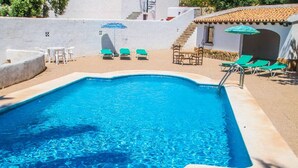Una piscina rectangular con agua azul cristalina, rodeada de sillas de descanso y sombrillas.