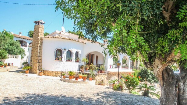 Un edificio blanco con chimenea de piedra, ventanas arqueadas y plantas en macetas.