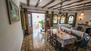 Un comedor con una mesa dispuesta para cuatro personas, sillas de madera y un banco. Hay una ventana con cortinas, una lámpara colgante y un cuadro en la pared.