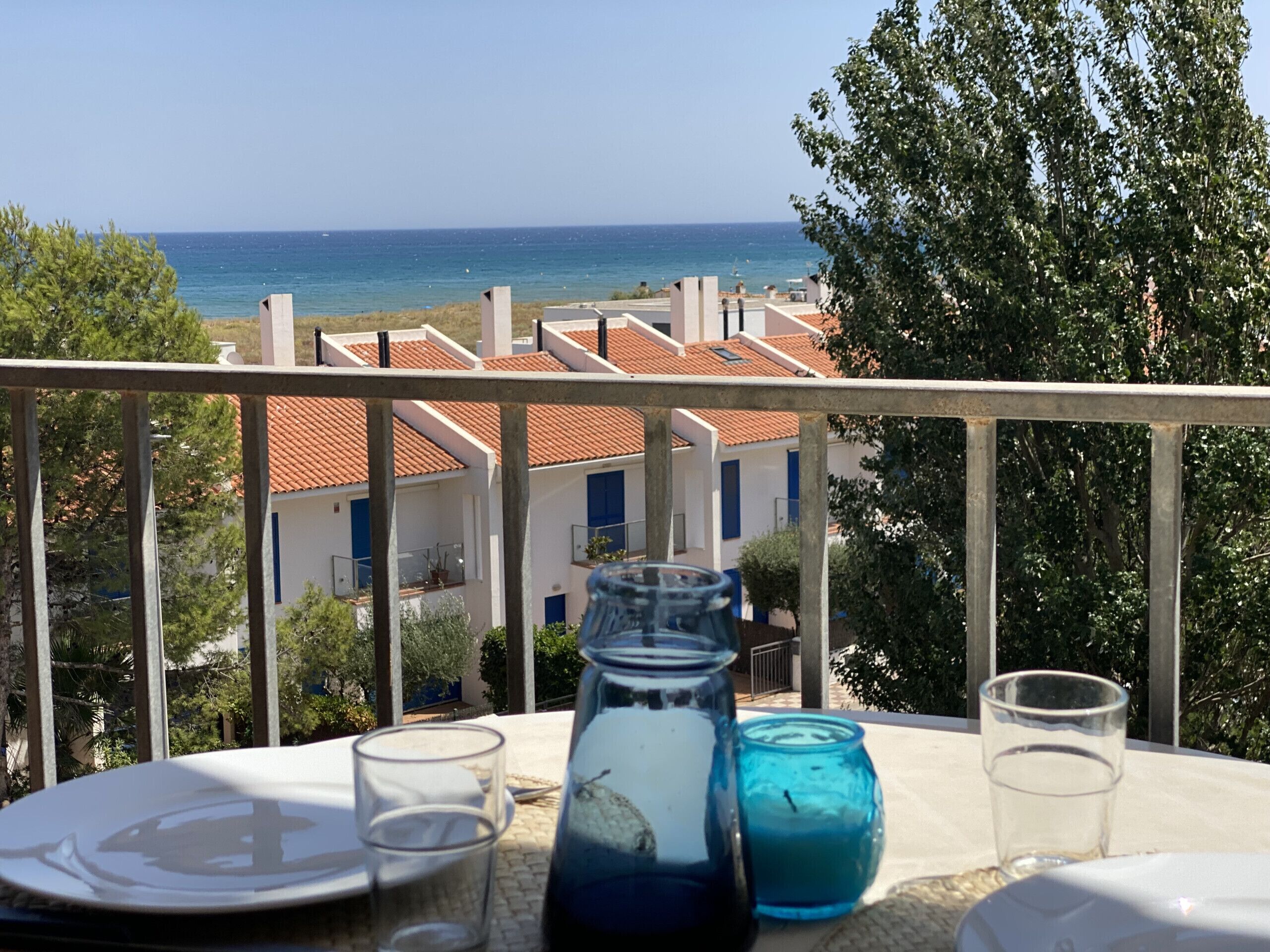 Ein Balkon mit Tisch für zwei Personen, der Blick ins Küstenlandschaft mit Gebäuden und Bäumen bietet.