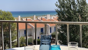 Un balcón con una mesa dispuesta para dos personas, con vistas a la costa, edificios y árboles.