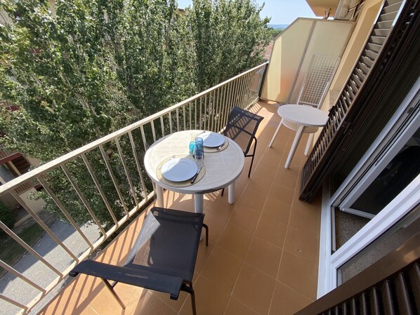 Un balcón con una mesa dispuesta para dos, una silla y un ventanal.
