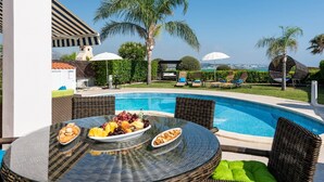 A poolside area with a table set for a meal, lounge chairs, and a view of the sea. - Villa Tequila Sunrise by Ezoria Villas (Coral Bay)