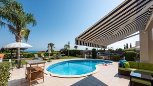 A pool area with a covered seating area, lounge chairs, and a view of the sea. - Villa Tequila Sunrise by Ezoria Villas (Coral Bay)