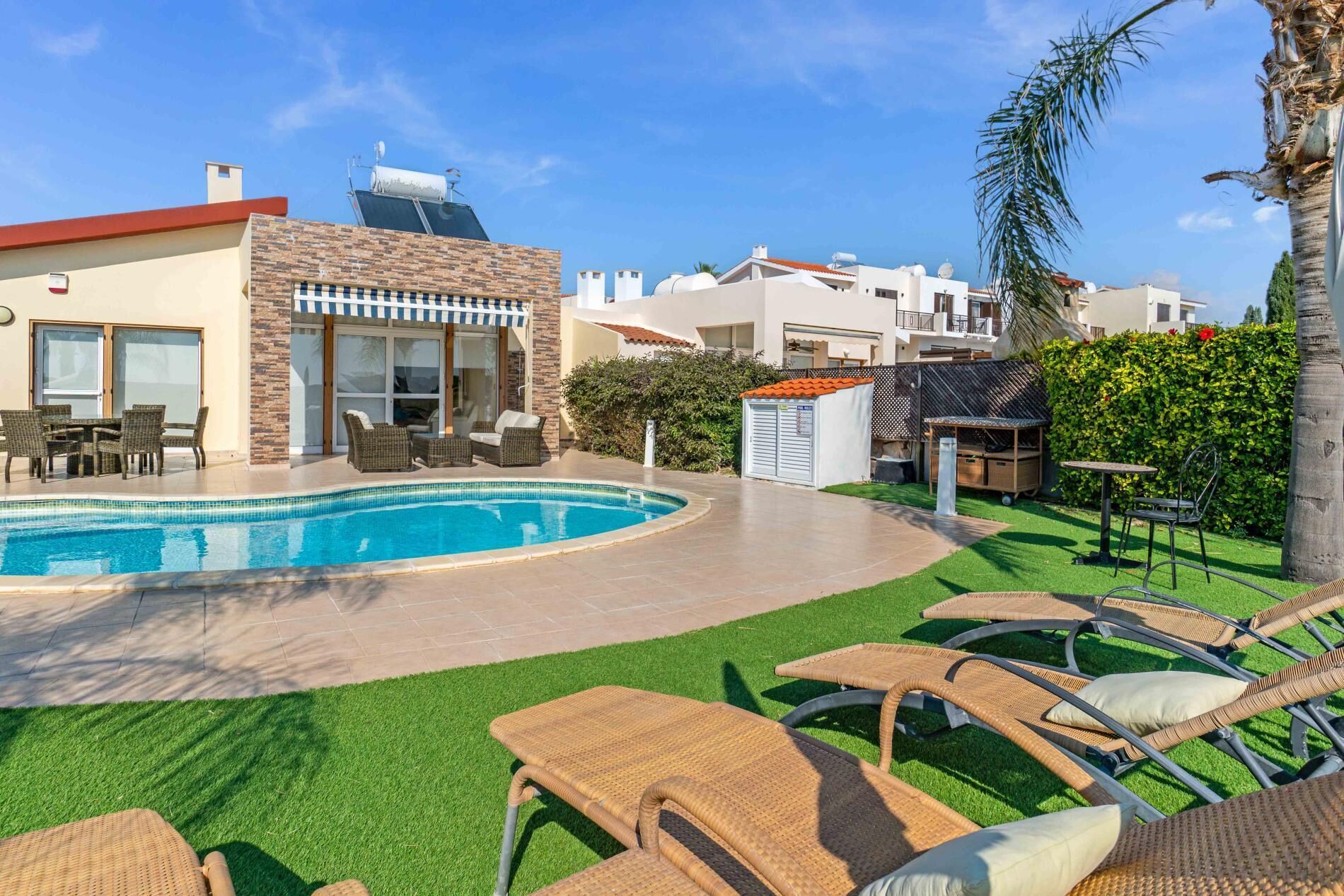 A pool area with a clear blue pool, wicker lounge chairs, and a small building with a red roof.