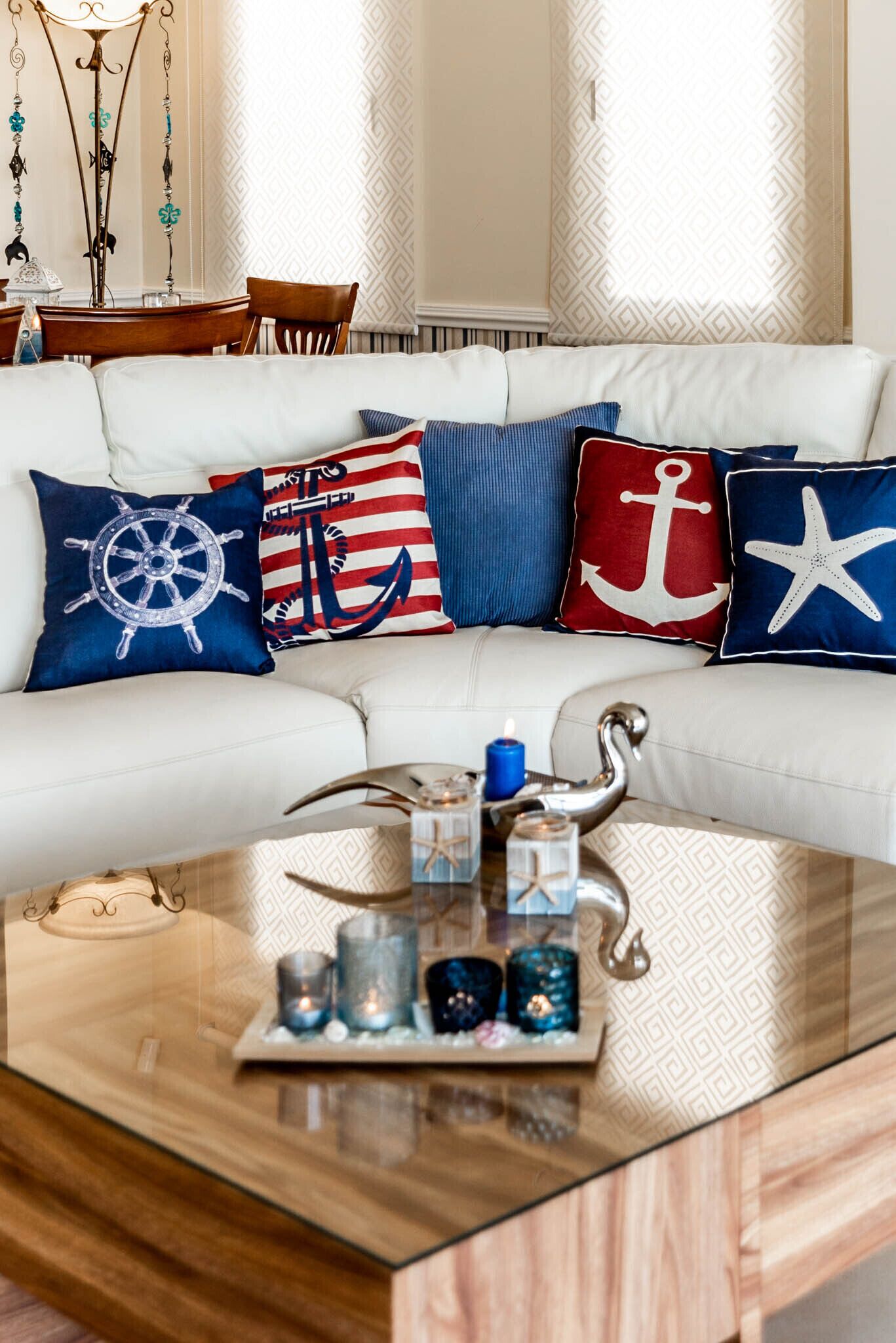 Een witte bank met marinekussens, een glazen salontafel met kaarsen en een decoratieve metalen zwaan.