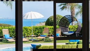 A room with a view of a pool and outdoor seating, a chandelier, and patterned wallpaper. - Villa Tequila Sunrise by Ezoria Villas (Coral Bay)