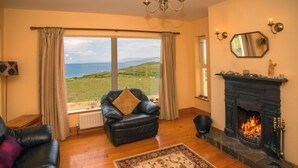 A cozy living room with a fireplace, a leather sofa, a black armchair, and a view of the sea. - Cottage 259 - Renvyle - sleeps 6 guests  in 3 bedrooms (Renvyle)