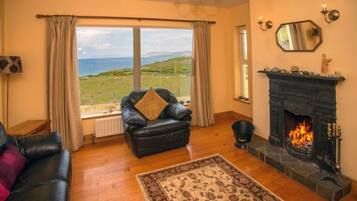 A cozy living room with a fireplace, a leather sofa, a black armchair, and a view of the sea.