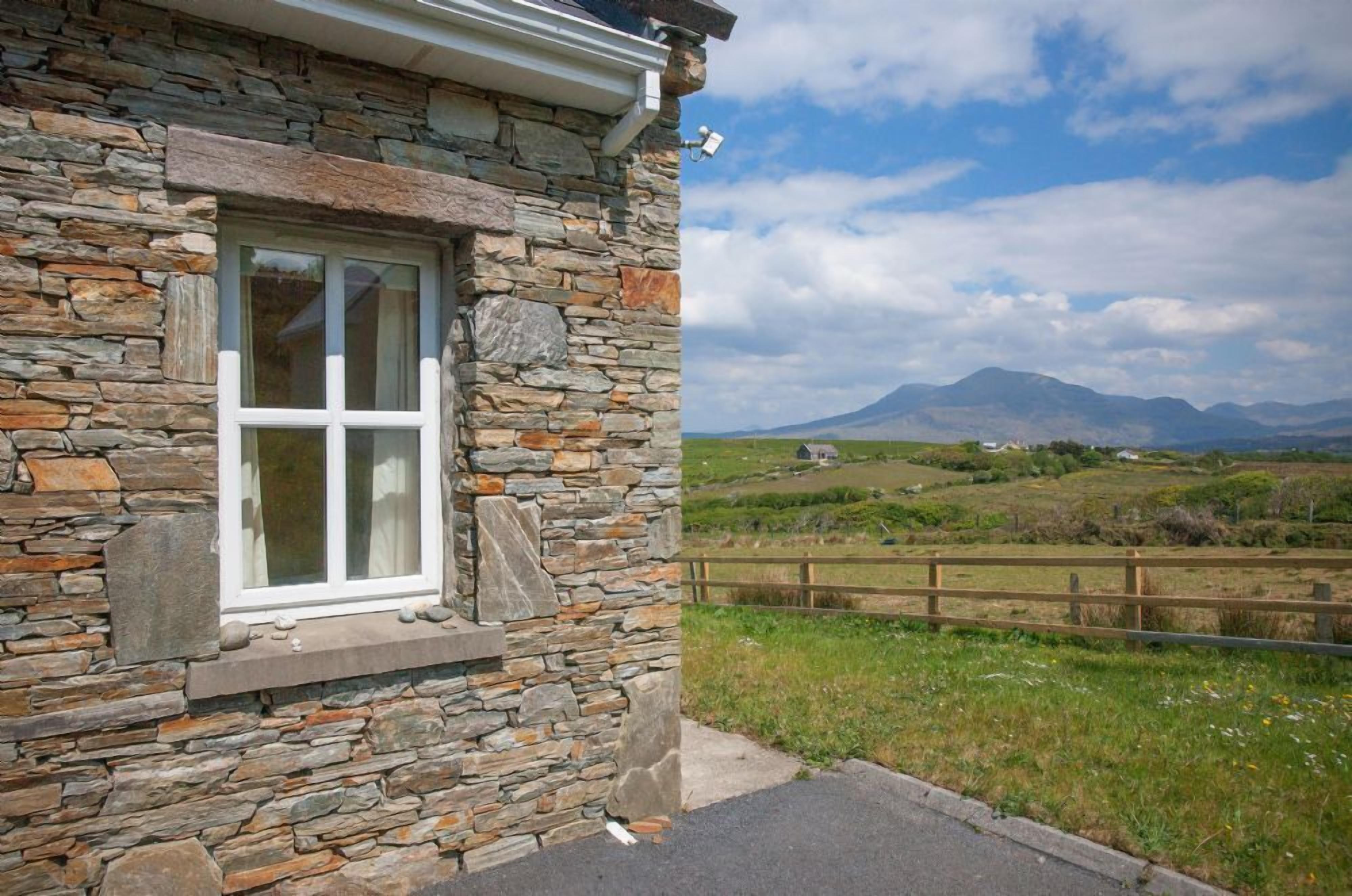 A stone building with a window and a view of a rural landscape with mountains.