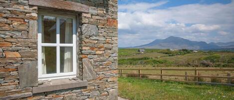 A stone building with a window and a view of a rural landscape with mountains.