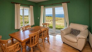 A room with a wooden dining table and chairs, a beige sofa with a patterned pillow, and a view of the outdoors through large sliding glass doors. - Cottage 259 - Renvyle - sleeps 6 guests  in 3 bedrooms (Renvyle)