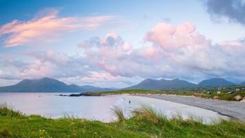 A coastal landscape with a road leading to a body of water, surrounded by grassy areas and distant mountains.