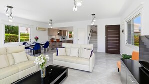 A modern living room with a sofa, coffee table, and dining area. - Villa Roker by Ezoria Villas (Coral Bay)