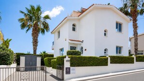 A white villa with a gated entrance, palm trees, and a clear sky. - Villa Roker by Ezoria Villas (Coral Bay)