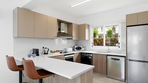 A modern kitchen with a central island, built-in appliances, and a window with a view of greenery. - Villa Roker by Ezoria Villas (Coral Bay)