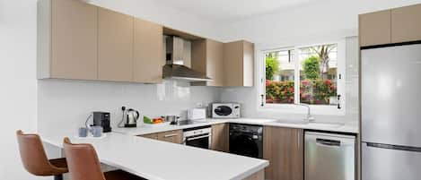 A modern kitchen with a central island, built-in appliances, and a window with a view of greenery.