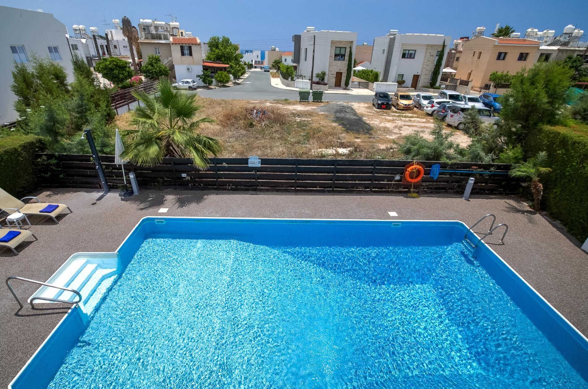 En swimmingpool med utsikt över bostadshus och parkerade bilar.