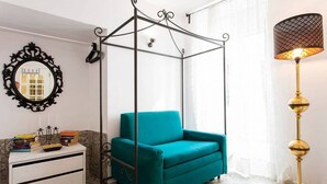 A room with a teal sofa, a white nightstand with books, a black-framed mirror, and a gold lamp. - JOIVY Calm 1-bed flat (Lisbon)