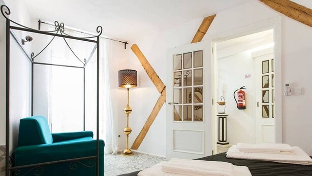 A hotel room with a bed, a blue chair, a standing lamp, and a door leading to another room. - JOIVY Calm 1-bed flat (Lisbon)